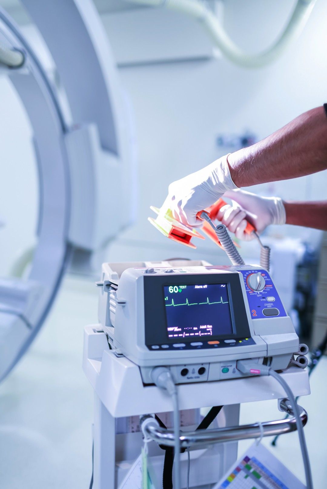 Clinician in surgical gloves operating a patient monitor beside medical imaging equipment