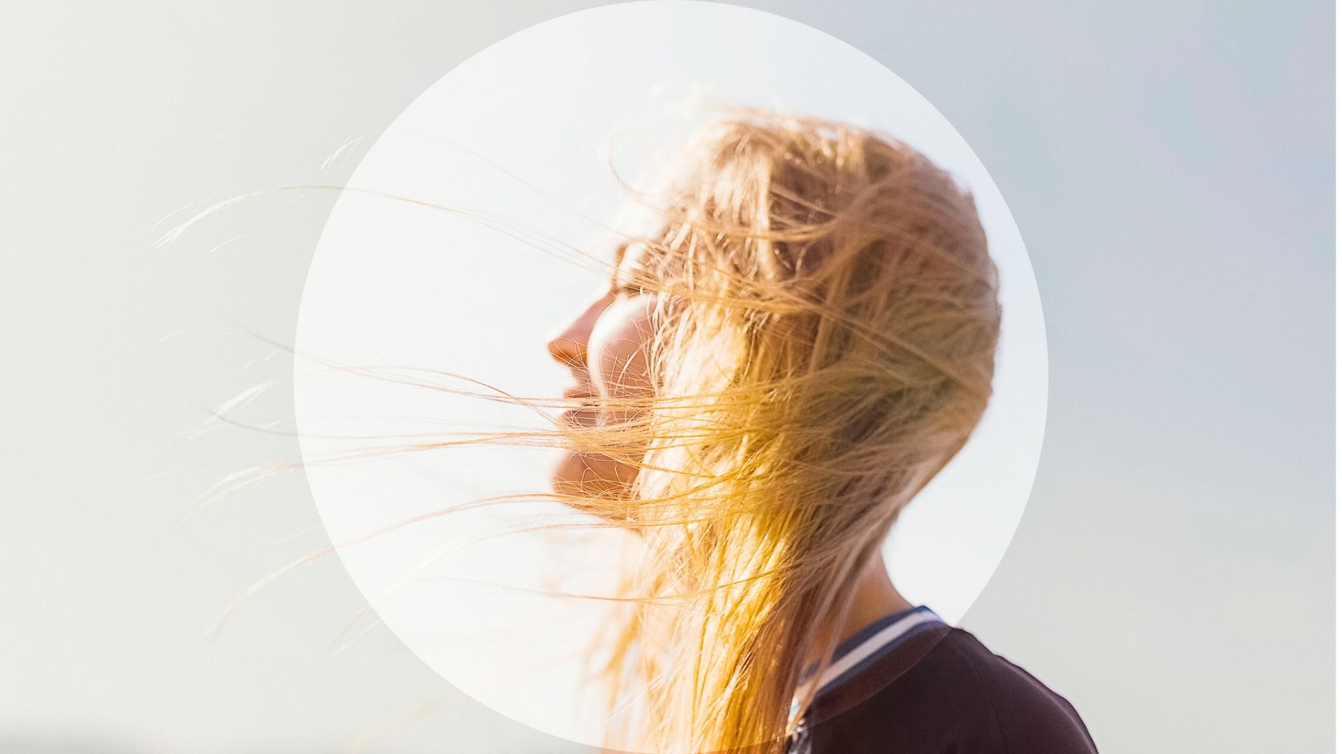 Woman standing outdoors with her hair blowing across her face in bright sunlight