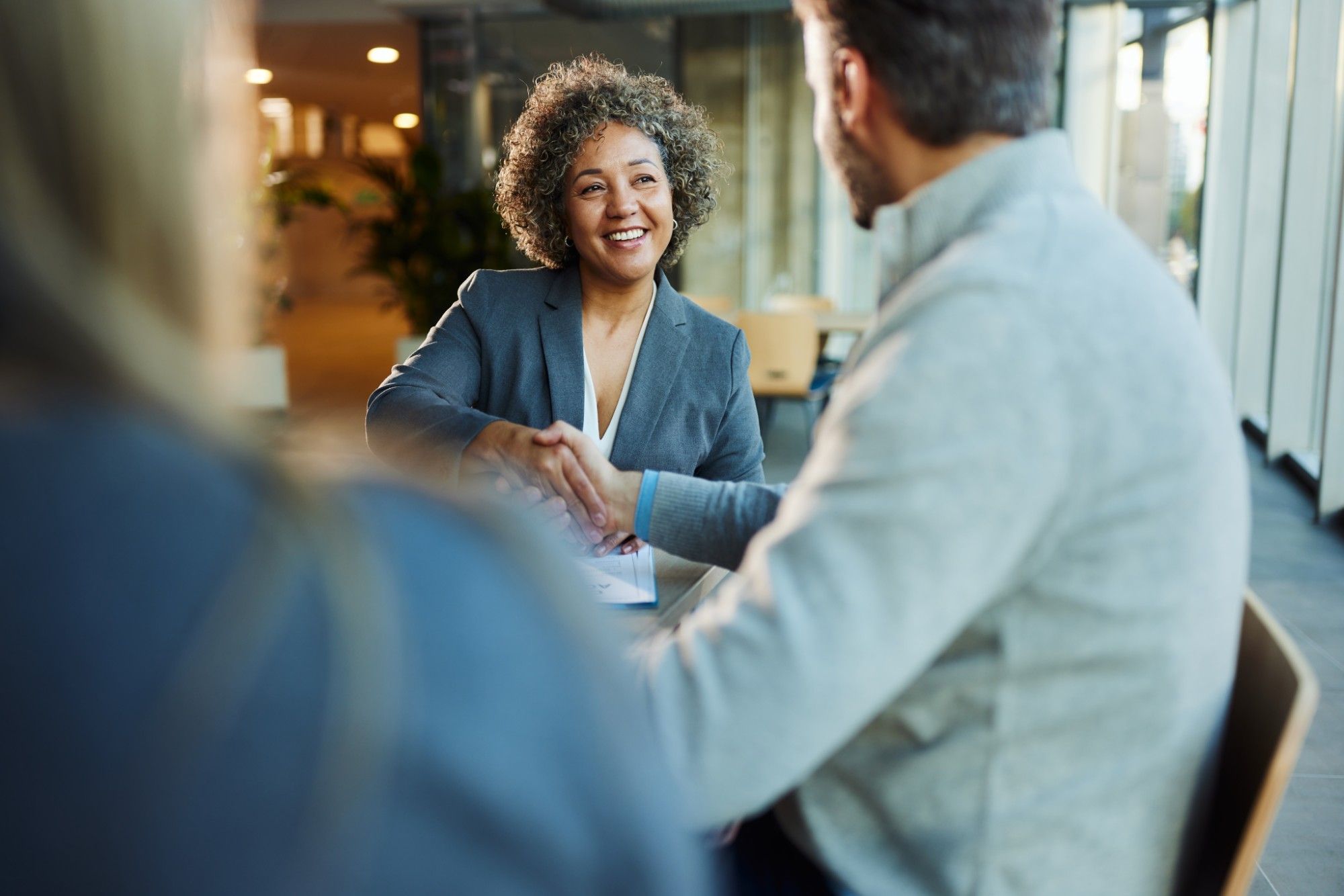 Smiling businesswoman in a blue blazer shaking hands with a male colleague across a meeting table