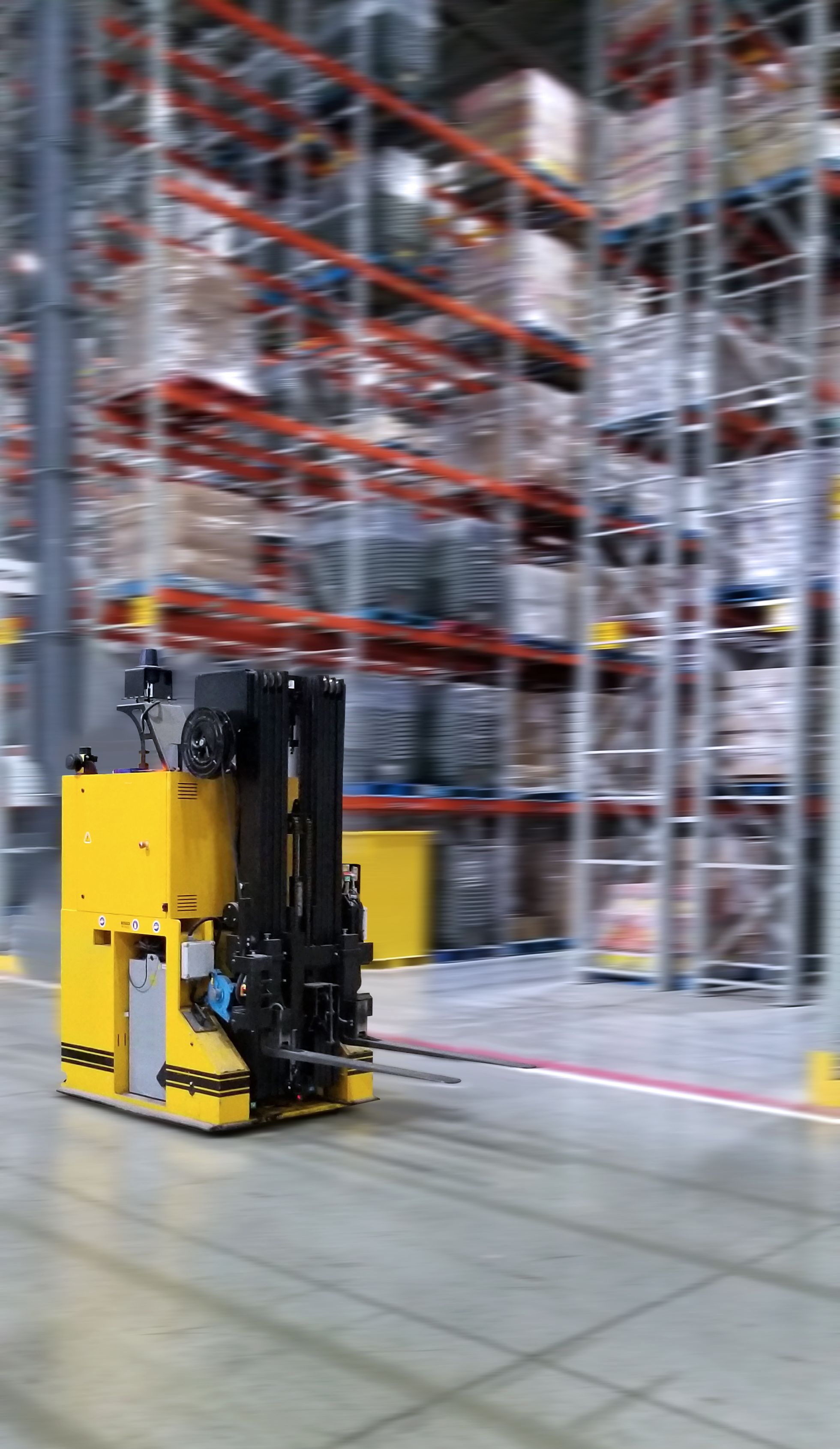An AGV forklift moving fast across a warehouse floor