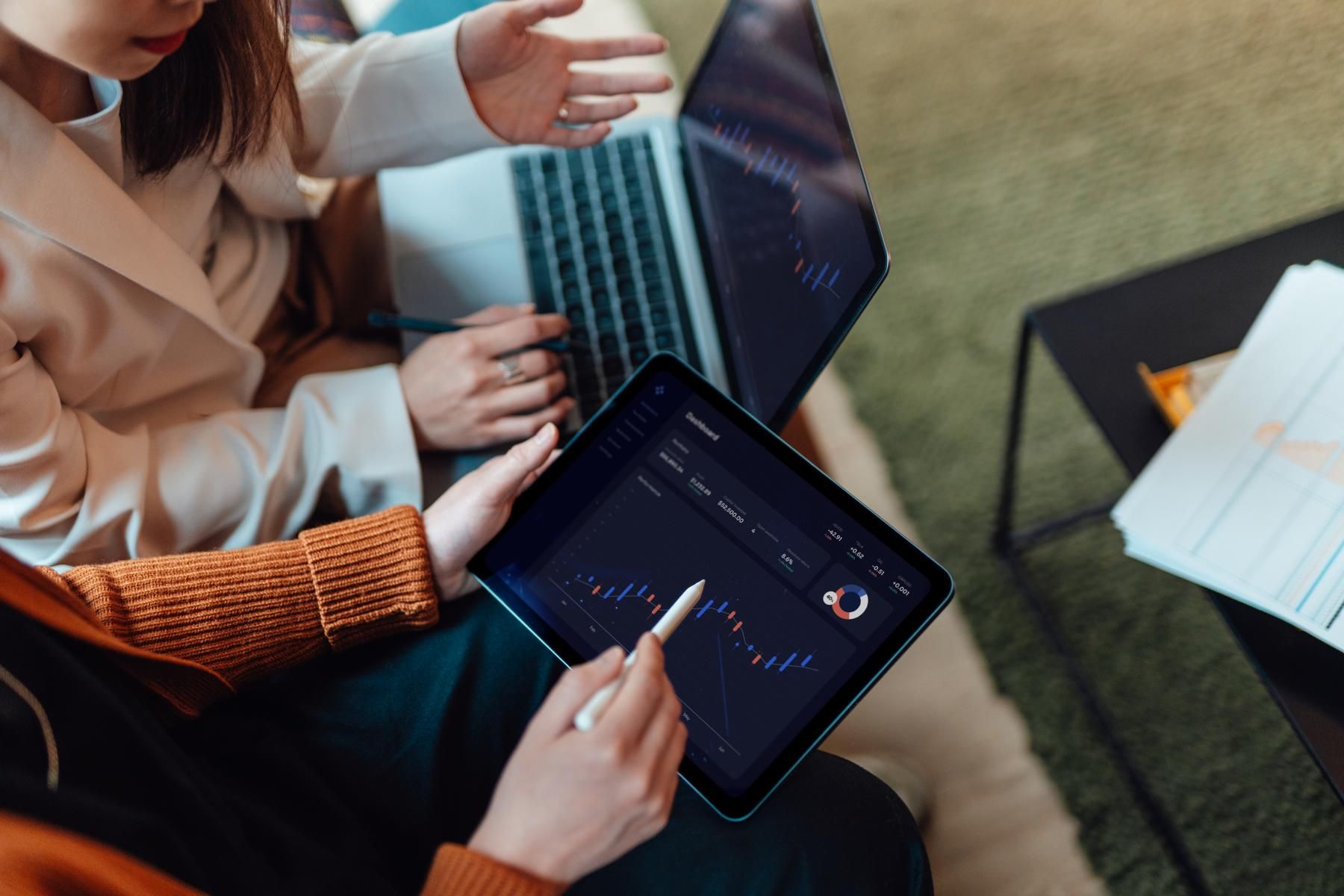 Two people working next to each other while holding a laptop and a tablet