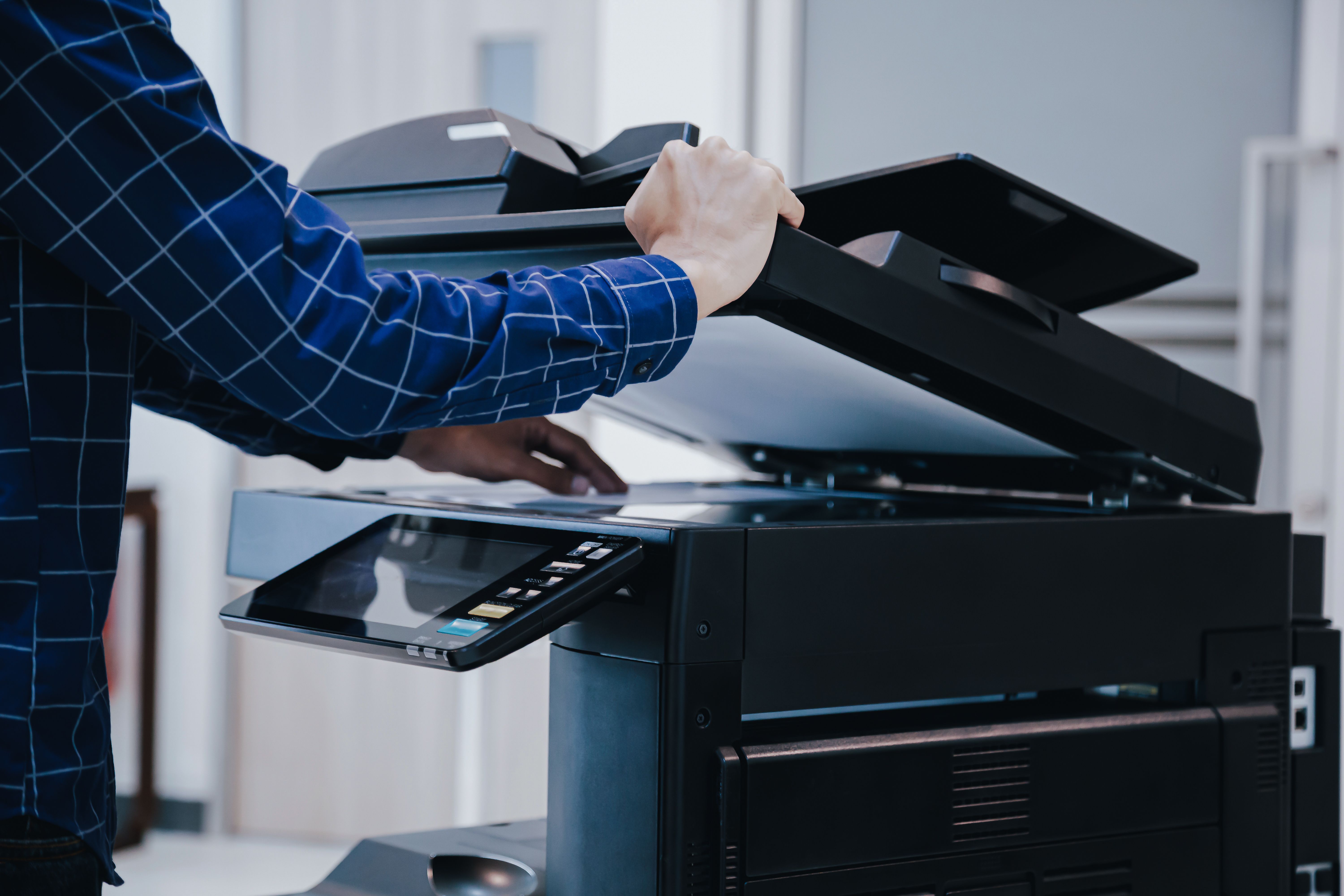 Close-up of a man in a plaid shirt lifting the lid of an office copier to scan a document