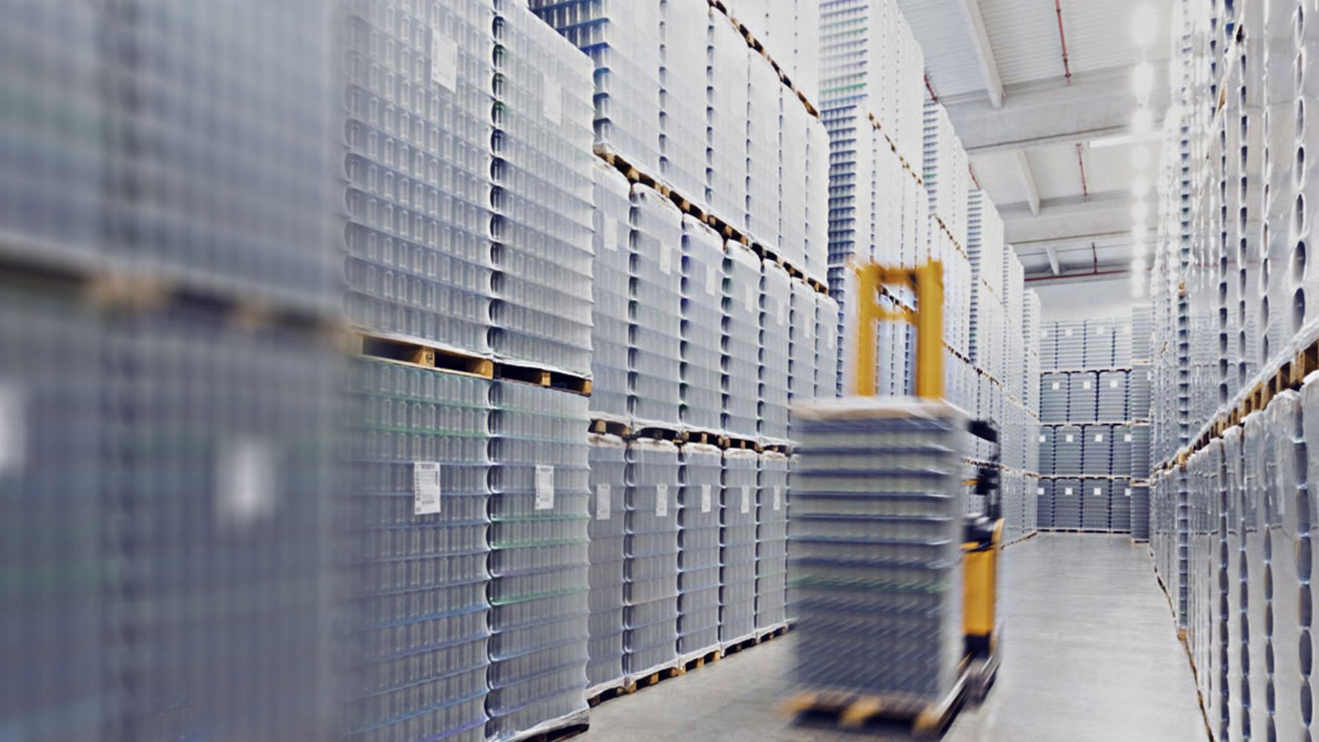 Automated material handling robot moving a packaged pallet down an aisle in a high-rack warehouse, illustrating fleet and TCO analysis for material handling equipment.