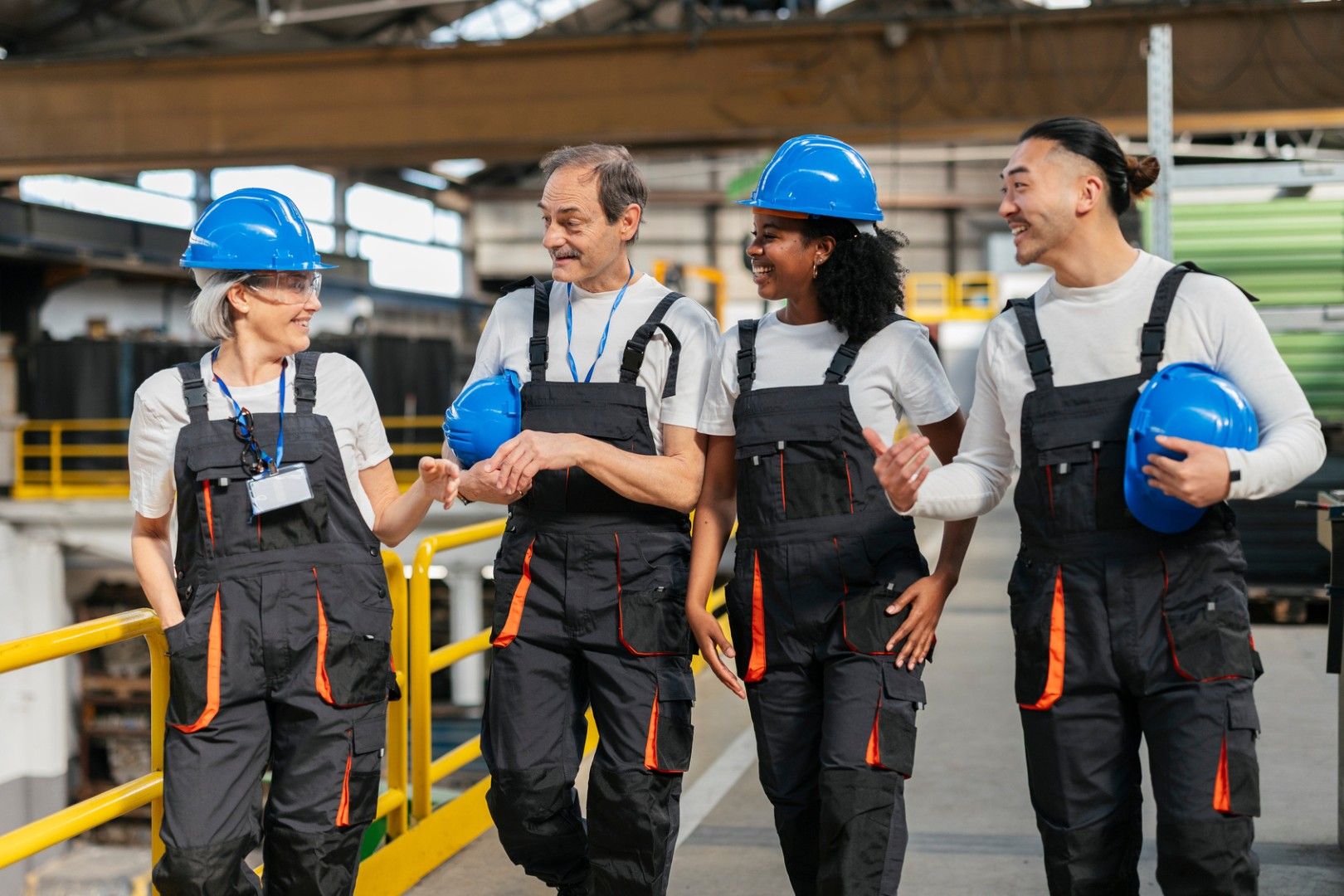 Four workers in identical overalls and blue hard hats walking together through a plant