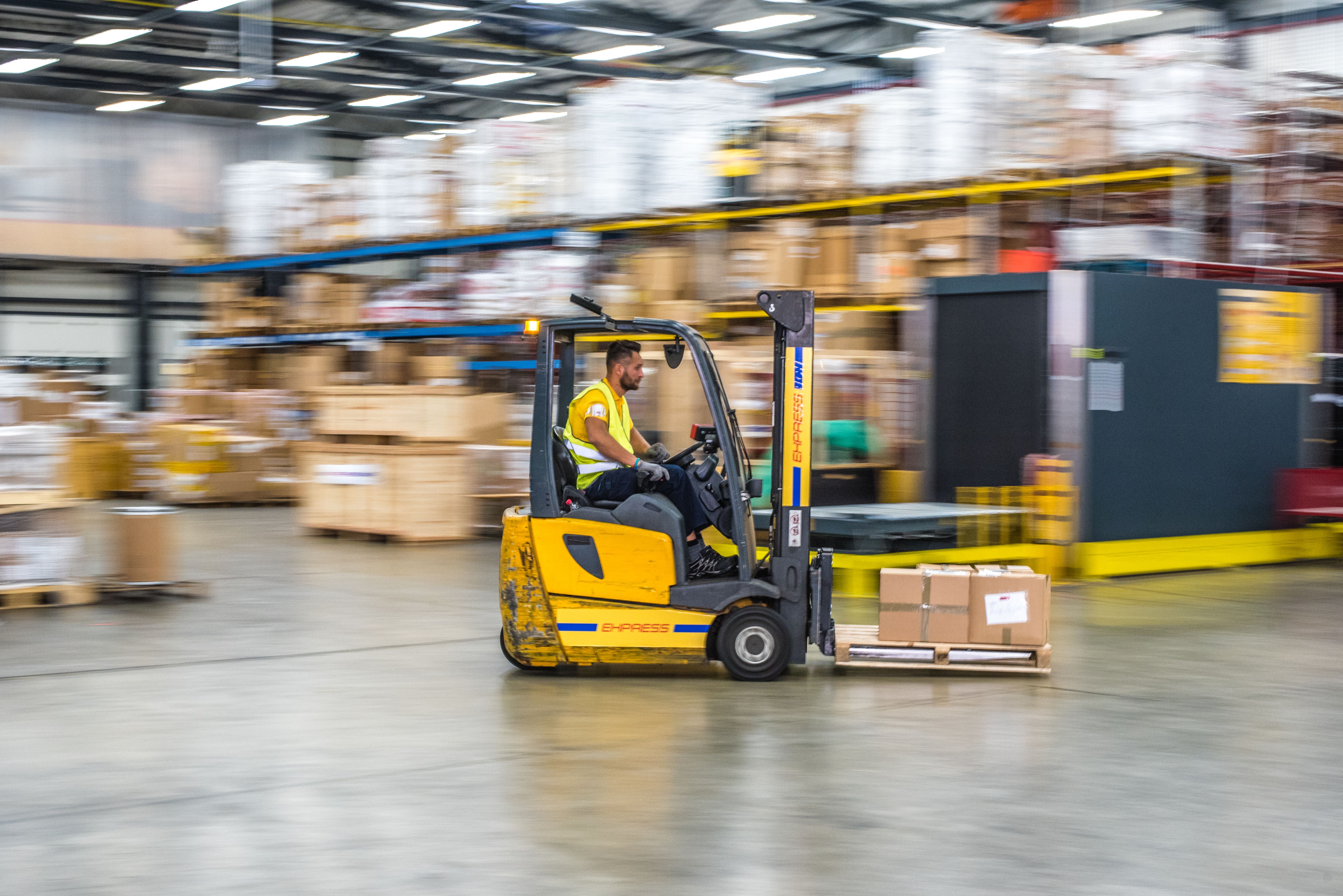 Forklift quickly moving across a warehouse floor while a man operates it.