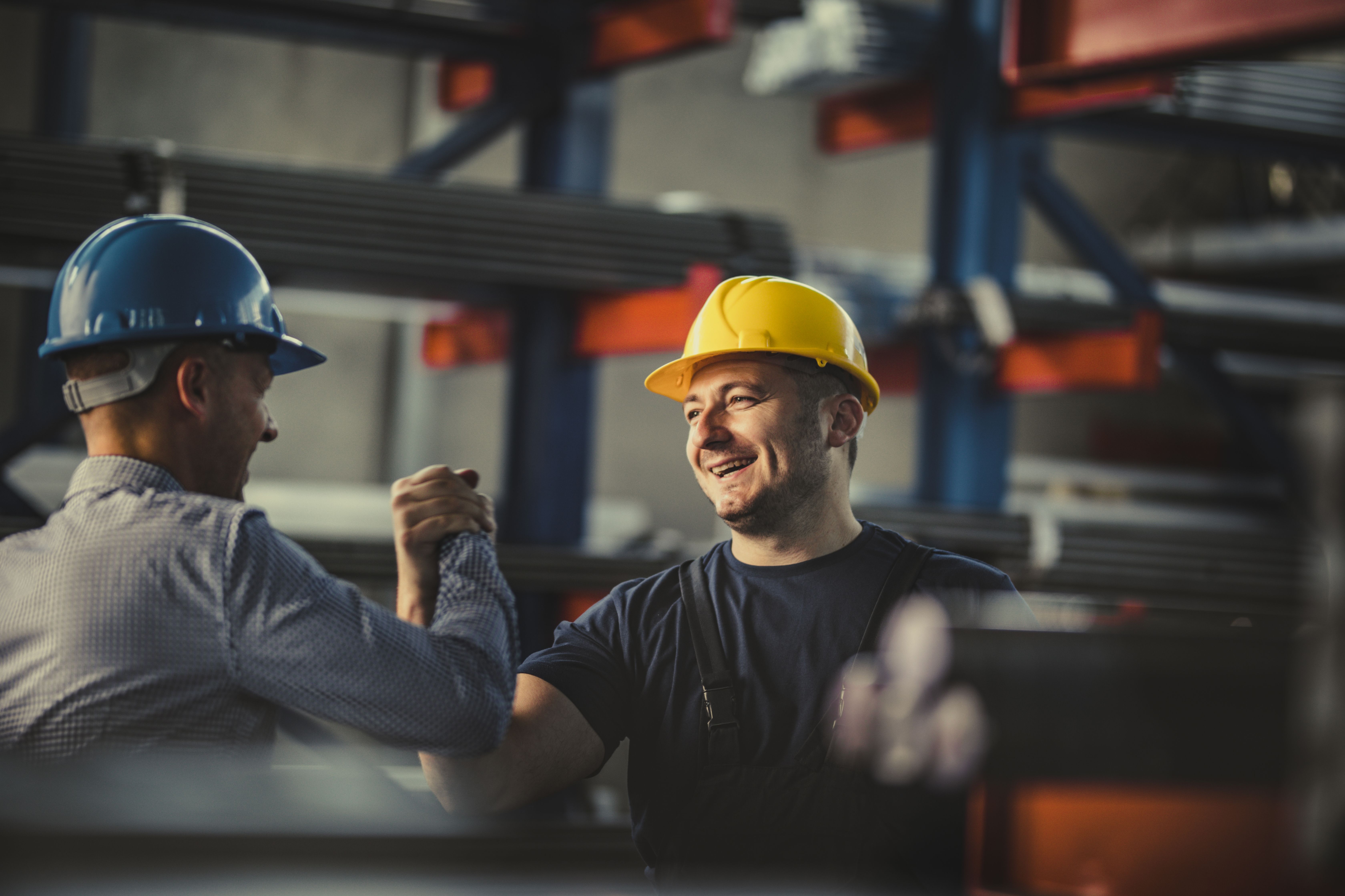 Two warehouse workers shaking hands and smiling wearing hard hats