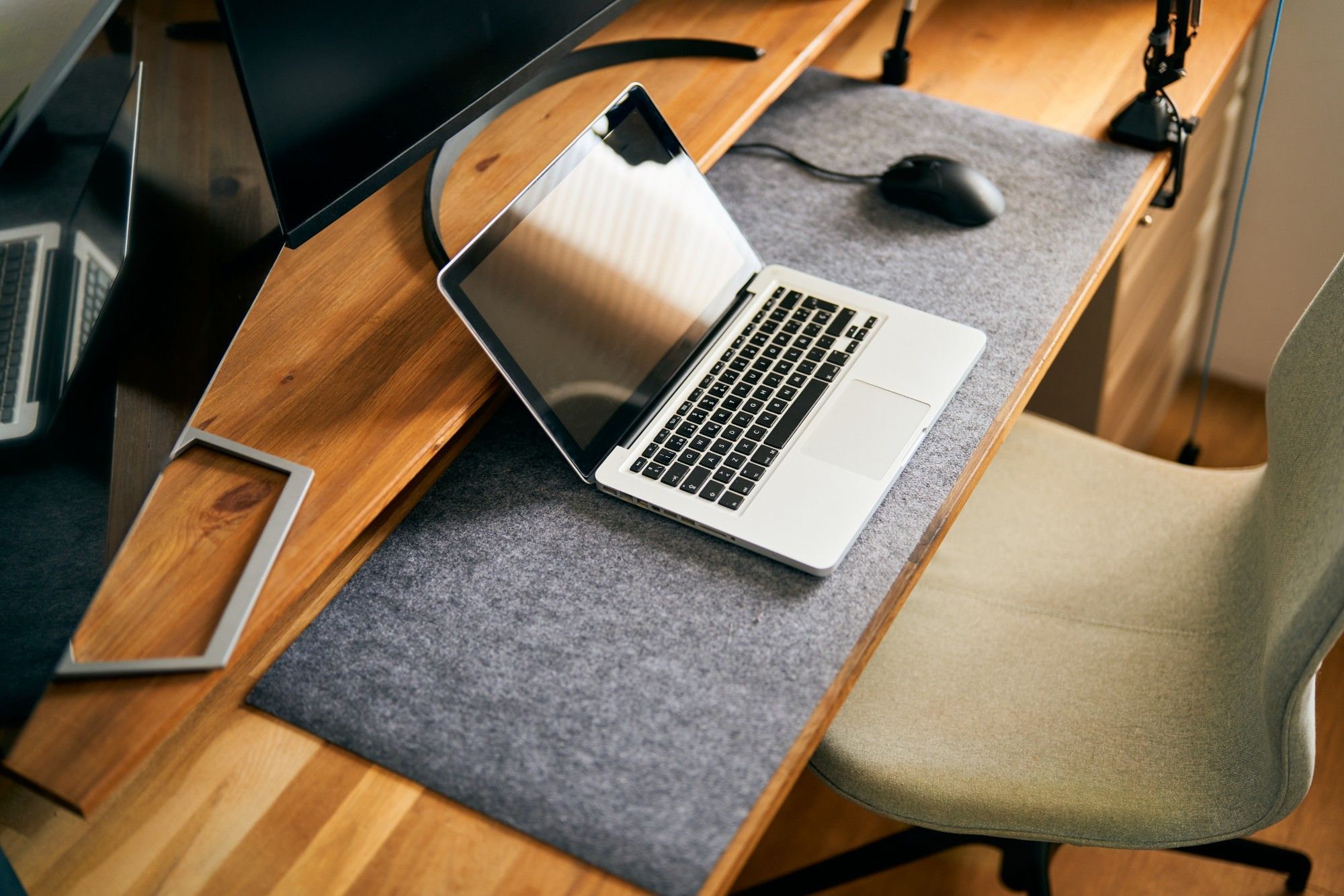 Overhead view of an open laptop and mouse on a felt desk mat in a home office with a wooden desk