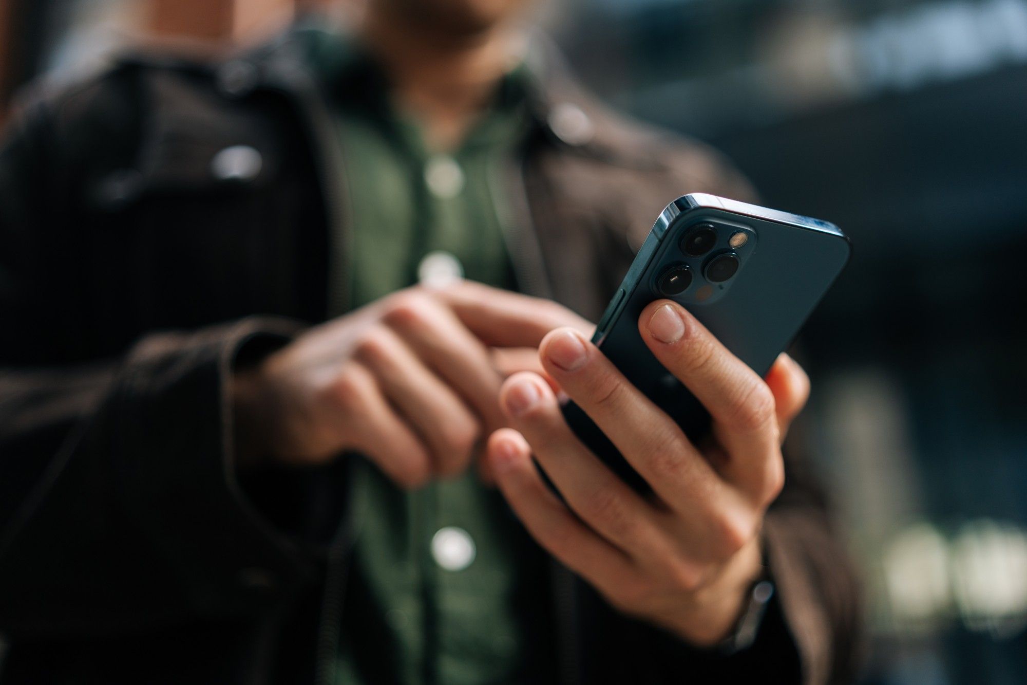 Close-up of a man in a dark jacket holding and tapping a company smartphone