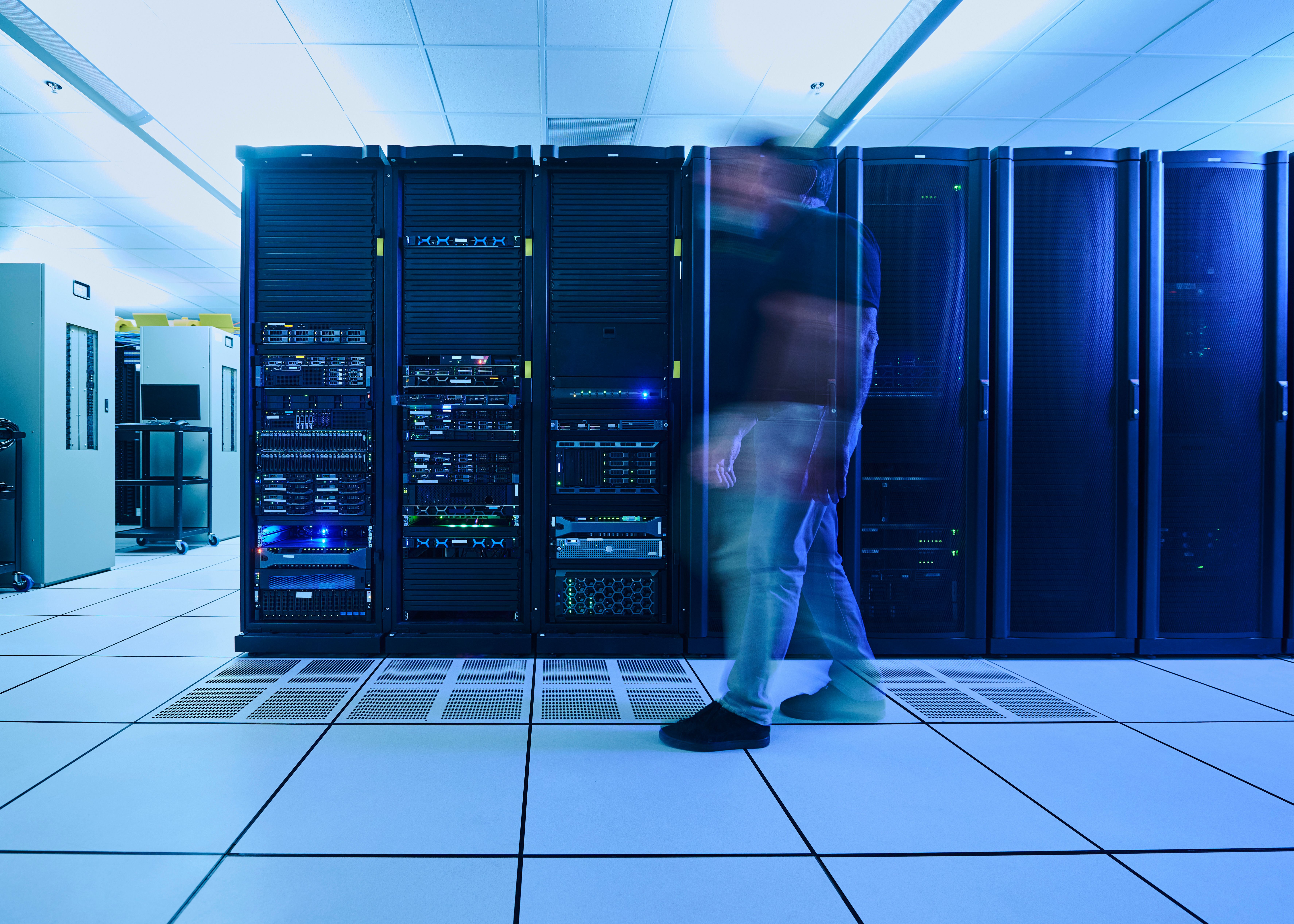 Technician walking past rows of server racks with blue status lights in an enterprise data center