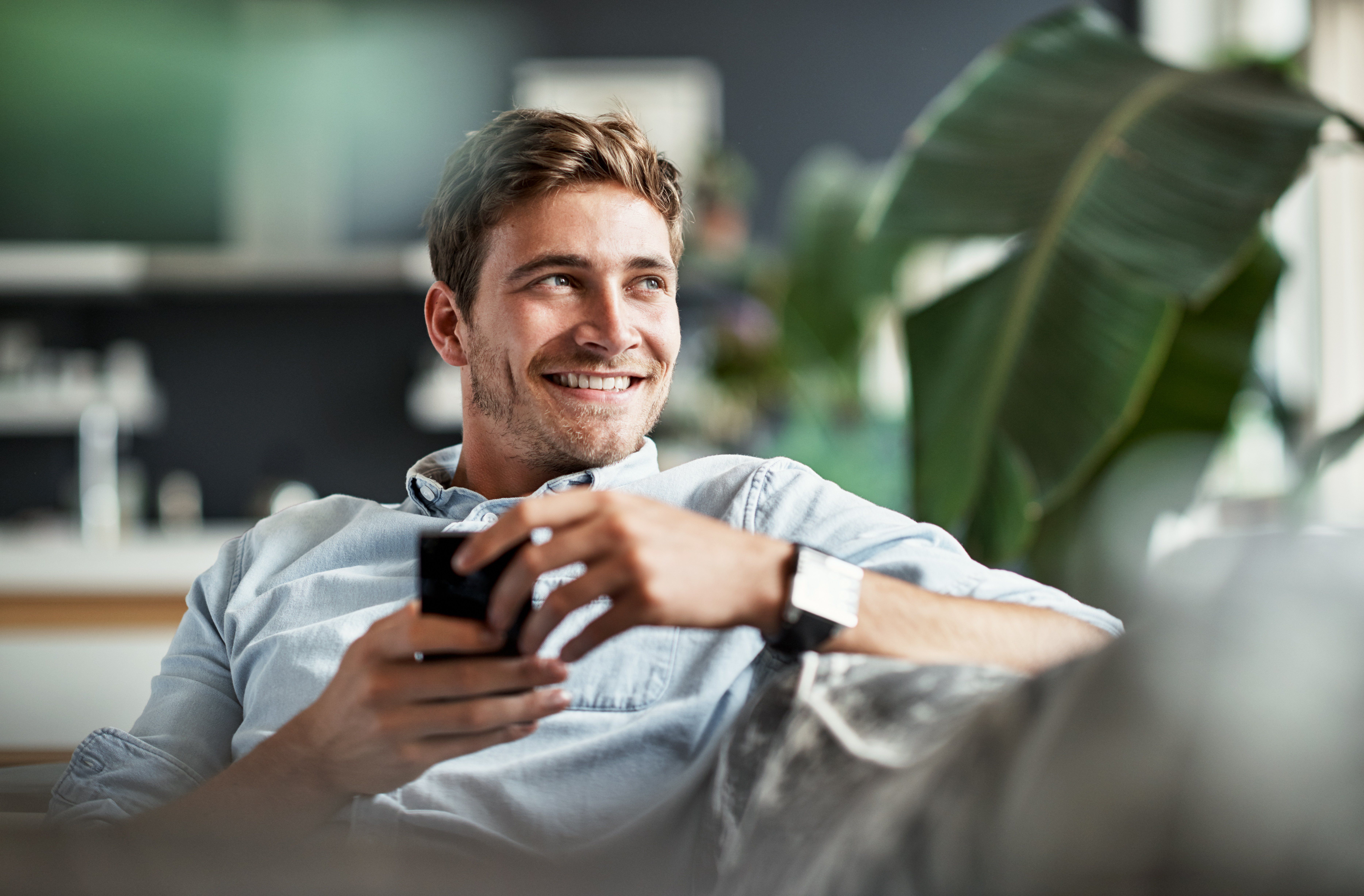 Caucasian man sitting on a couch and smiling while looking out a window