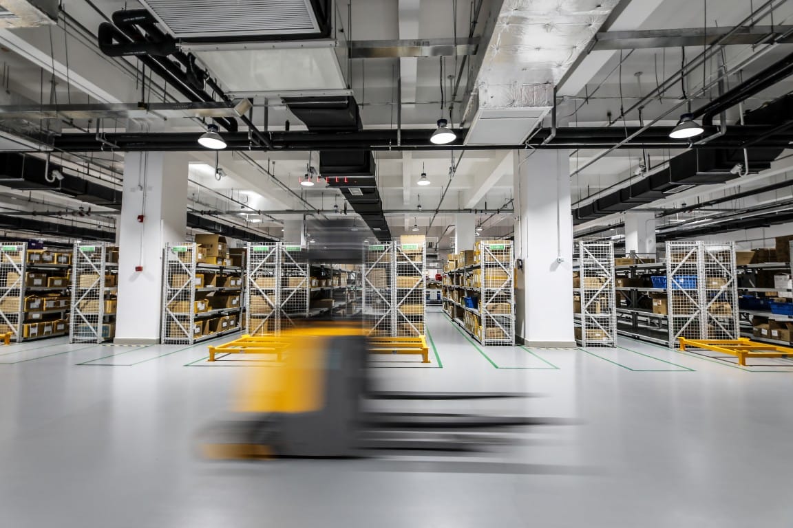 Warehouse interior with tall pallet racking and a motion-blurred forklift moving down the aisle
