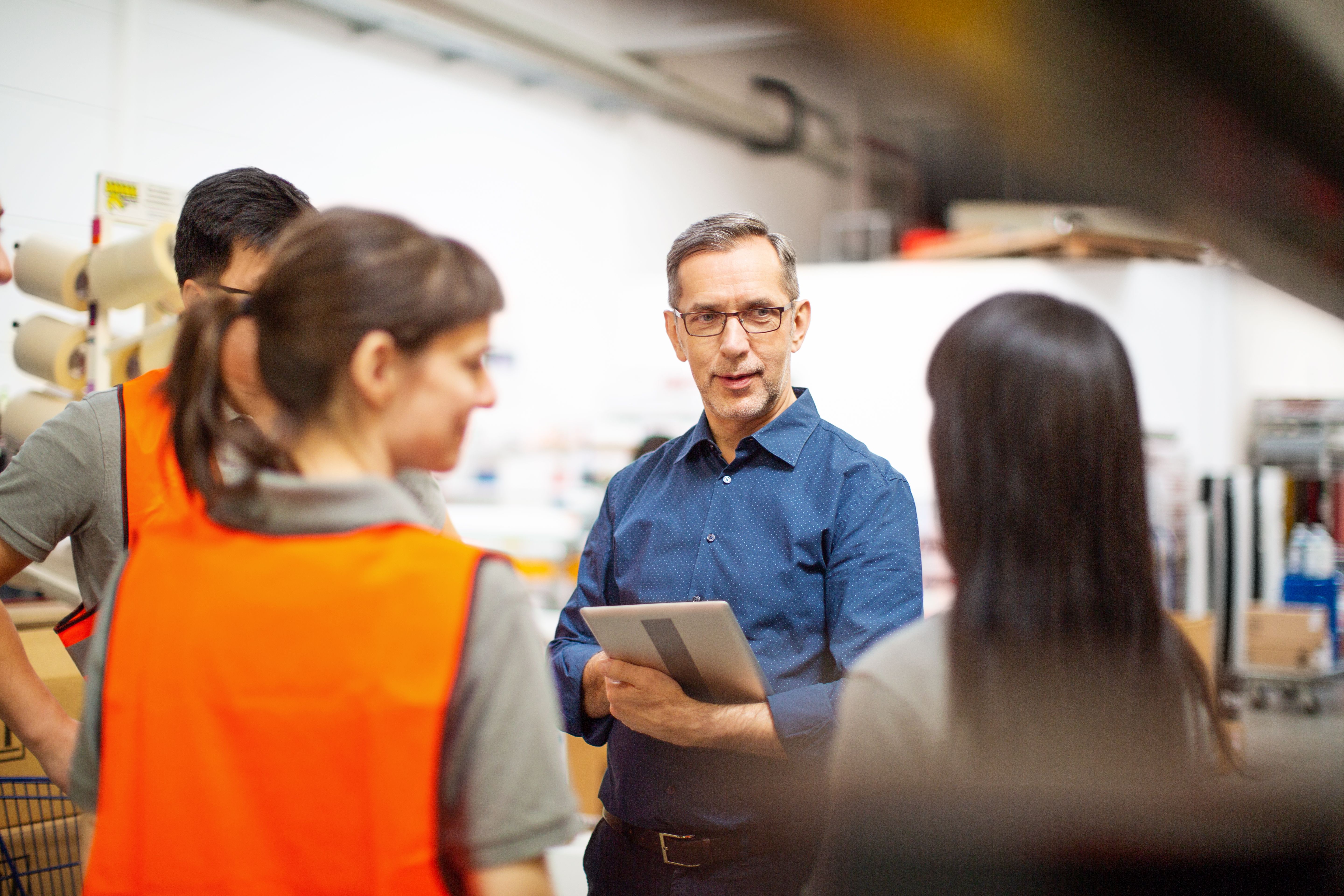 Four people in a warehouse having a conversation while the leader holds and ipad