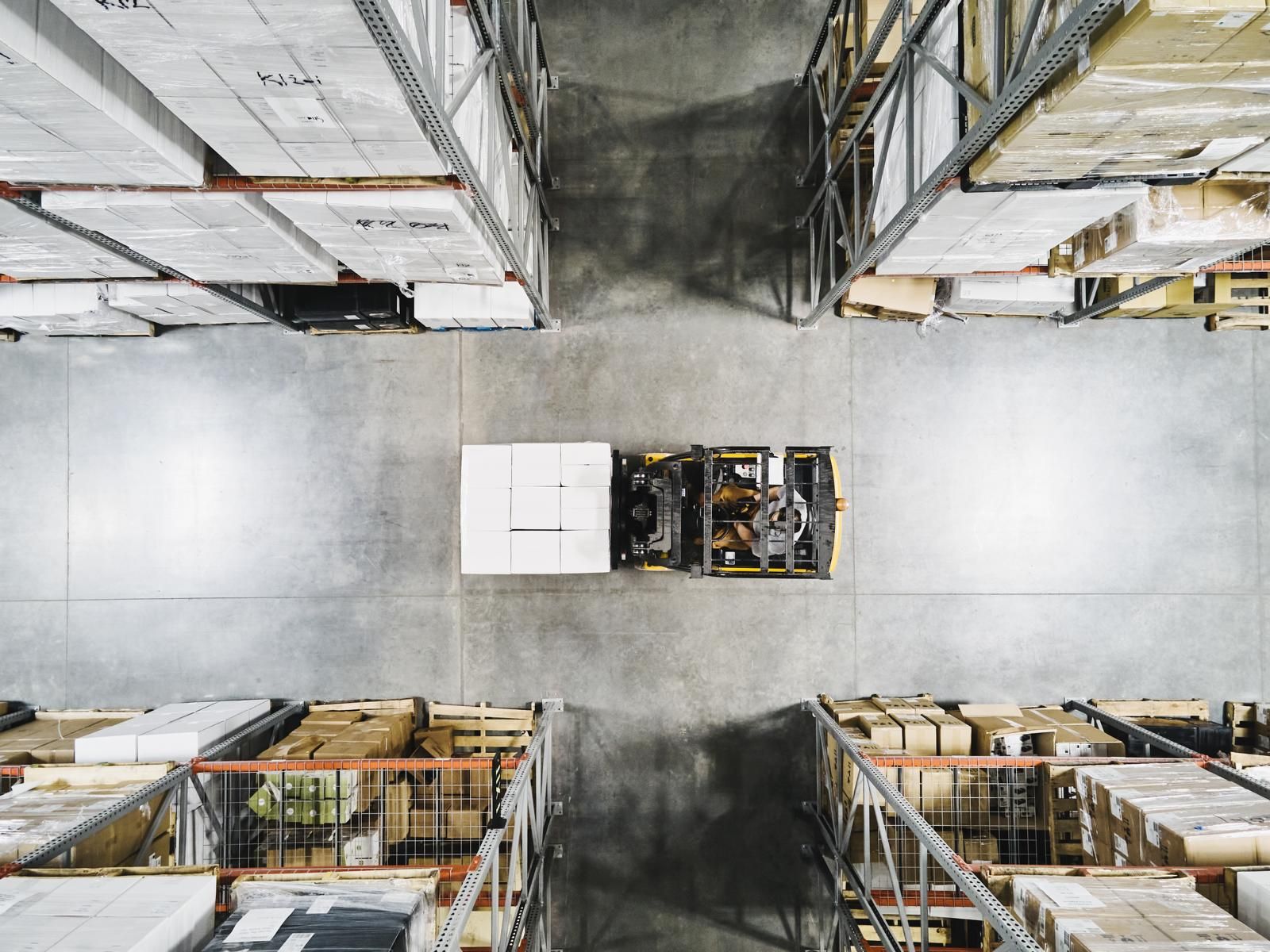 Overhead view of a forklift carrying a pallet down a warehouse aisle between storage racks