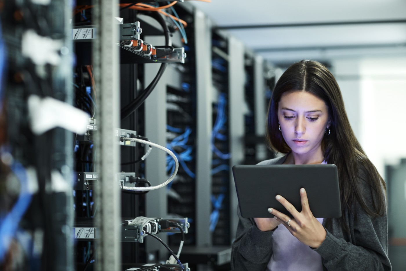 IT technician using a tablet next to a server rack with network cables in a data center