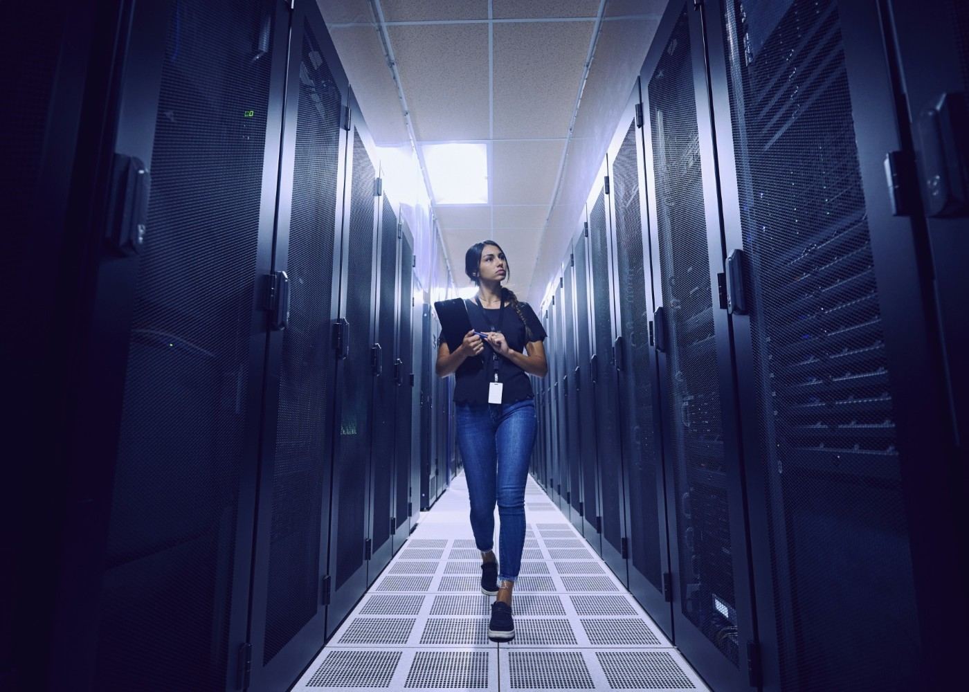 IT engineer holding a tablet while walking down a blue-lit aisle of server racks in an enterprise data center